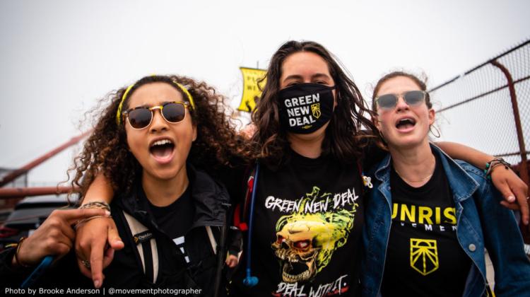 Three Sunrise Movement activists wearing black and yellow clothing that says "Green New Deal"