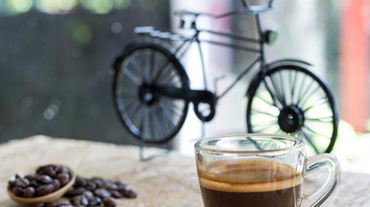 A cup of coffee in the foreground with an old fashioned bicycle in the background