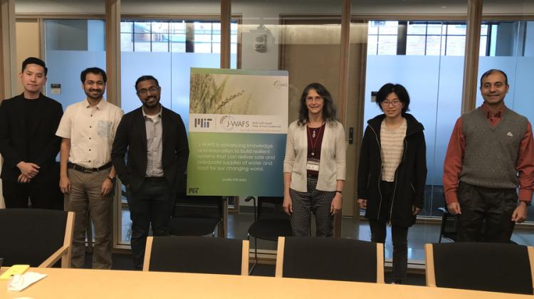 A group of six people standing in a conference room, posing for a photo beside a J-WAFS sign
