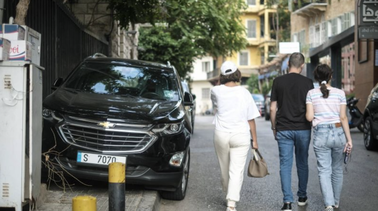 Image shows pedestrians walking in the middle of the street in Beirut, to the left of the image a car is parked on the sidewalk.
