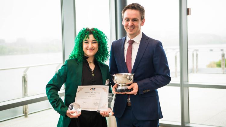 Two individuals pose with multiple awards in their hands