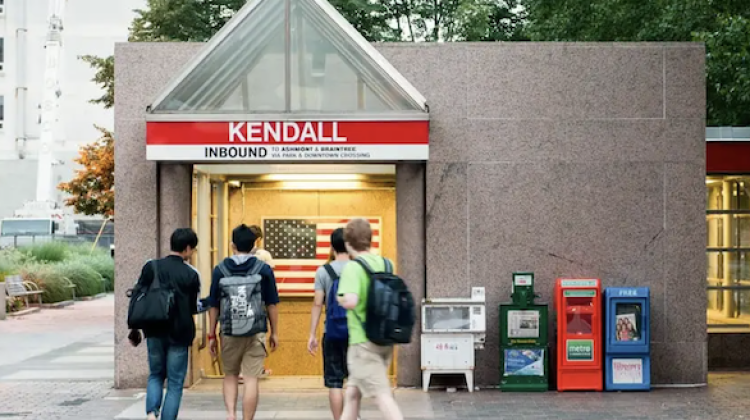 Four individuals, with backpacks, entering an entrance to the Kendall Square Red Line stop.