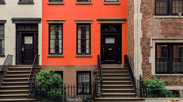 Image of row homes with various paint colors applied to their brickwork. On the far right of the image is an attached dwelling that is noticeably more detailed with stone work. 