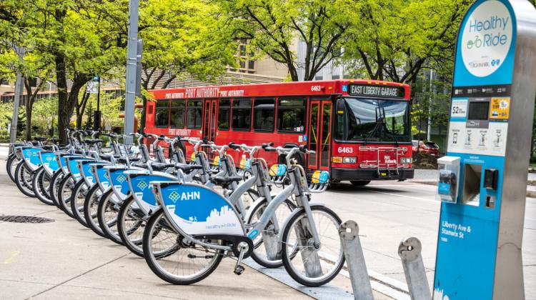 Pittsburgh, Pennsylvania, USA- May 12, 2021: Healthy Ride bike share station with red public bus passing in the background