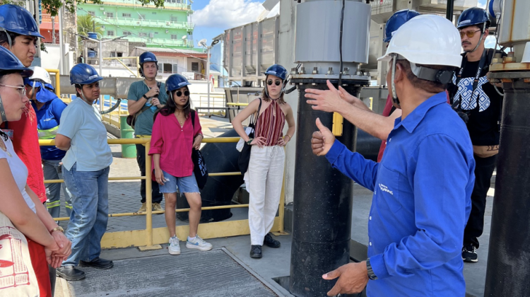 Individuals gather around a central speaker outdoors, all wearing safety helmets