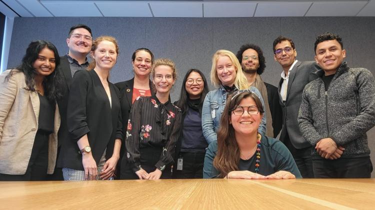 Group photo of students gathered at the end of a boardroom table, taken from a phone resting on said table