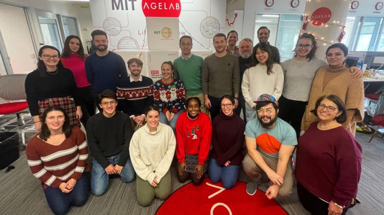 20 members of the Agelab pose for a group photo in the office, with the red AgeLab logo on the wall and on a rug.