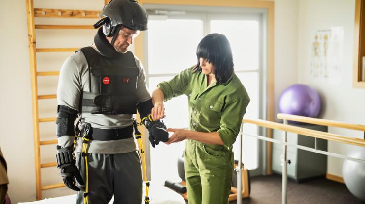 Actor Chris Hemsworth (on the left) is outfitted in the MIT AgeLab's AGNES suit on a recent episode of “Limitless With Chris Hemsworth.” To his right a MIT AgeLab team member adjusts the suit.