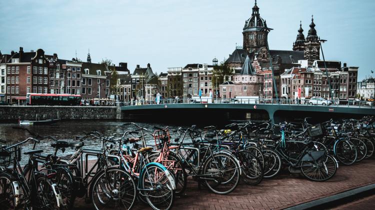 Image of bikes stored on a bike rack along the sides of a canal, in the distance classic Dutch row homes line the other side of the canal