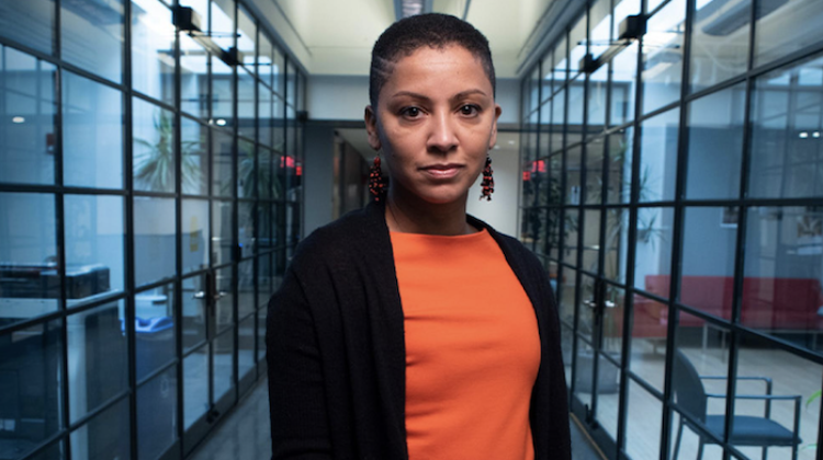 A hero style photo of Karilyn Crockett, standing in a glass wall hallway on MIT's campus (building 9, floor 5)