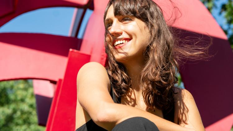 Jaye smiles while sitting down, with a red sculpture in background