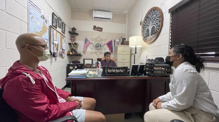 Shows a meeting between Mayor Rudy Aguon Paco, Kevin Lujan Lee, and Ngoc Phan. Lee and Phan are closer to the viewer, while Paco sits behind a desk in their office. 