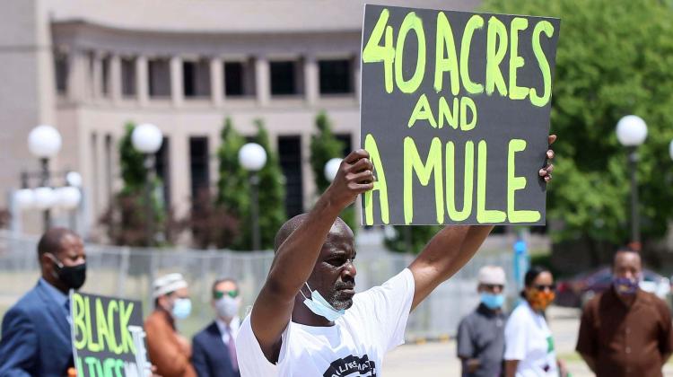 A protestor holds up a sign which reads, "40 acres and a mule," referencing the name - and material goods - by which the end of the civil war era reparation efforts attempted to make amends for generations of slavery