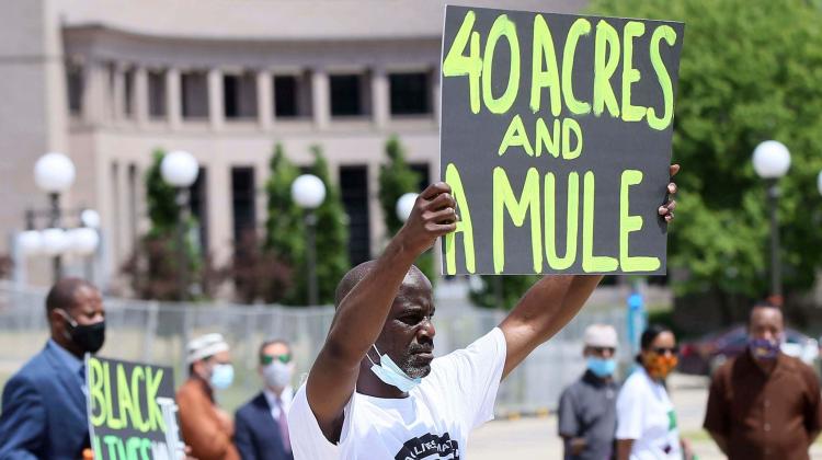 A protestor holds up a sign which reads, "40 acres and a mule," referencing the name - and material goods - by which the end of the civil war era reparation efforts attempted to make amends for generations of slavery  