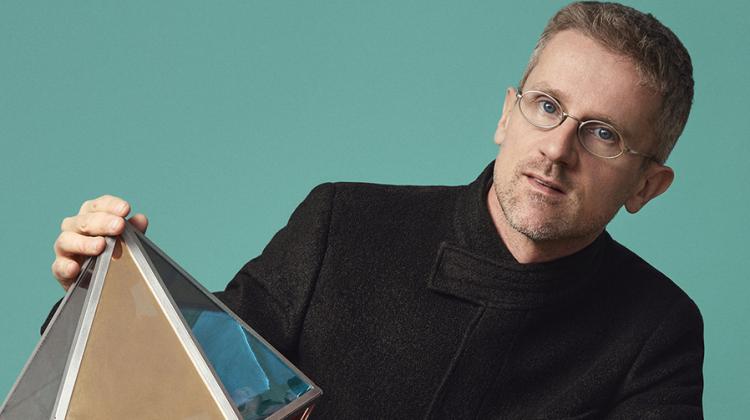 Carlo Ratti poses in a teal room with a geometric figure balanced on his knee