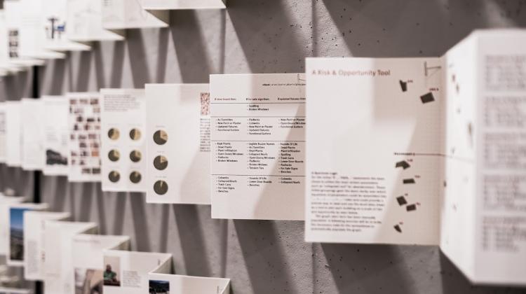 Photo of booklets that are part of the exhibition Rebuilding the Edge, viewers can see four booklets, unfolded and stretched across the length of a wall. The angle of the shot allows for details of the first few pages to be read, while subsequent pages are out of the focal length.