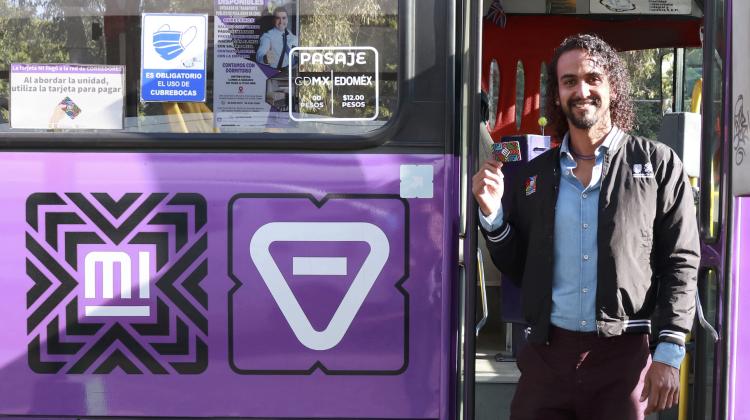 Image of Sanchez standing at the entrance to a bus, in their right hand they hold up an electronic fare key card.