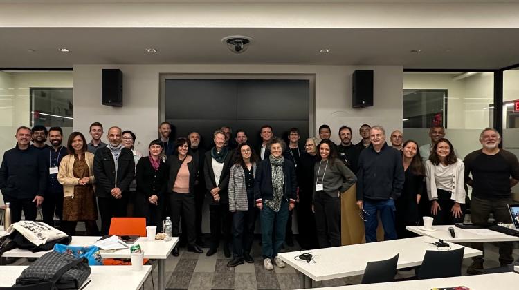 Group photo of participants of Urban Ground Floors, folks are assembled in front of the display of 9-255, desks/tables can be seen in the foreground