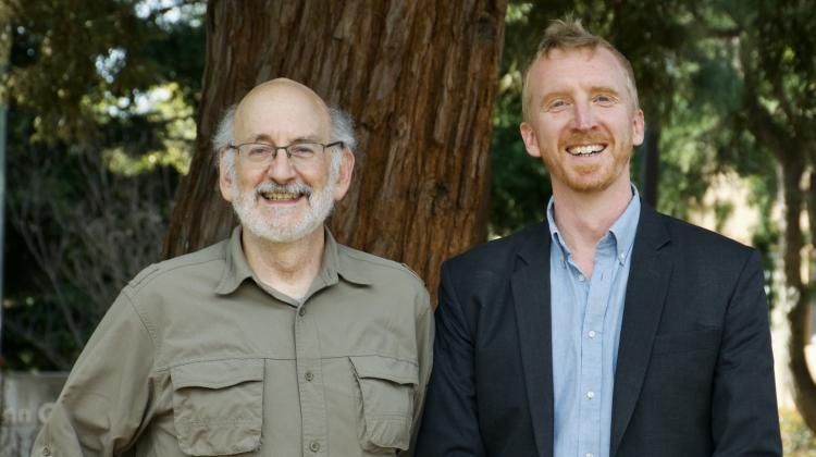Two individuals pose in front of redwood trees