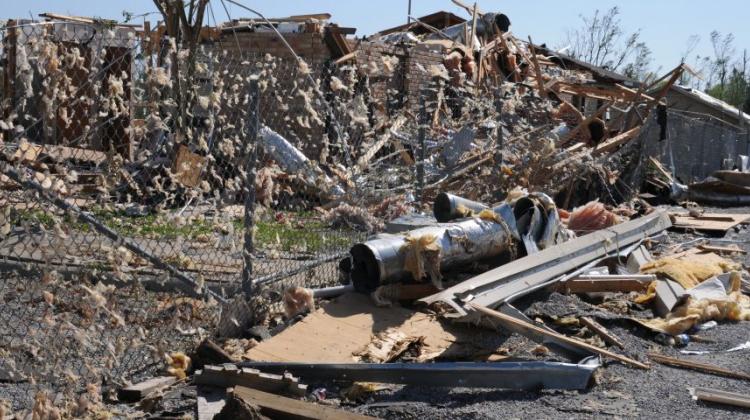 Image showing the aftermath of a tornado strike in an urban area, detritus is strewn across and through a chain link fence 