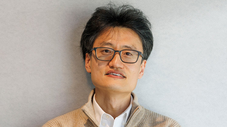 Jinhua Zhao wears a tan sweater and white collared shirt